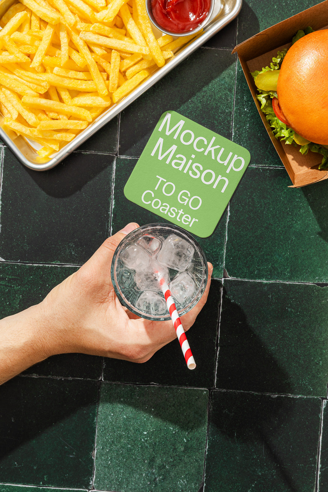 PSD mockup of a green coaster reading “Mockup Maison TO GO Coaster” next to a tray of fries, a burger, and a hand holding a glass with ice and a straw.