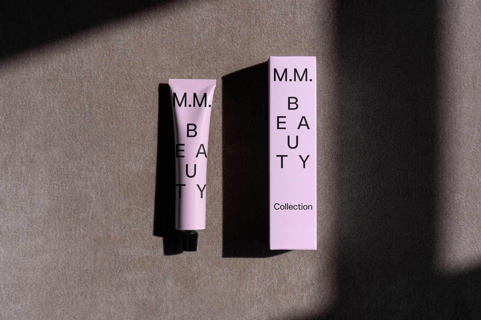 PSD mockup of a pink beauty tube and box with the label "M.M. Beauty Collection" on a textured surface.