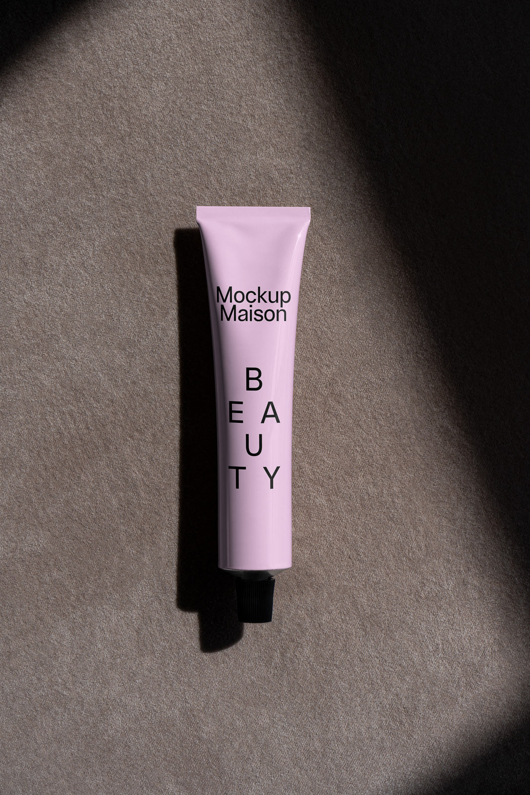 PSD mockup of a pink beauty product tube with black cap, labeled "Mockup Maison Beauty," placed on a textured, shadowed fabric surface.