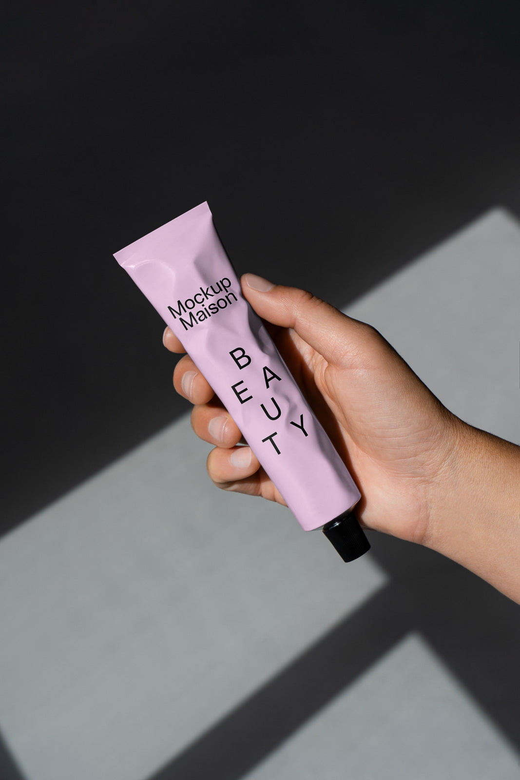 PSD mockup of a hand holding a lavender beauty tube labeled "Mockup Maison Beauty" against a dark background.