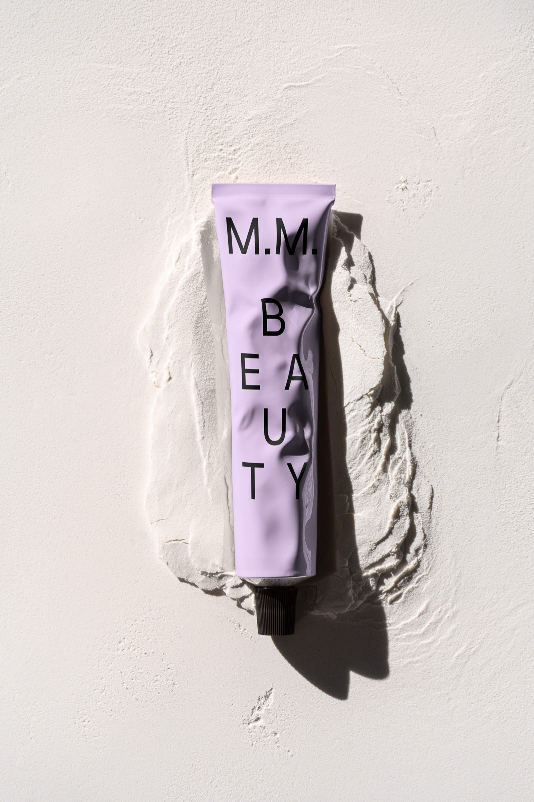 PSD mockup of a lavender beauty product tube with black cap on textured white surface, surrounded by sculpted plaster for an artistic presentation.