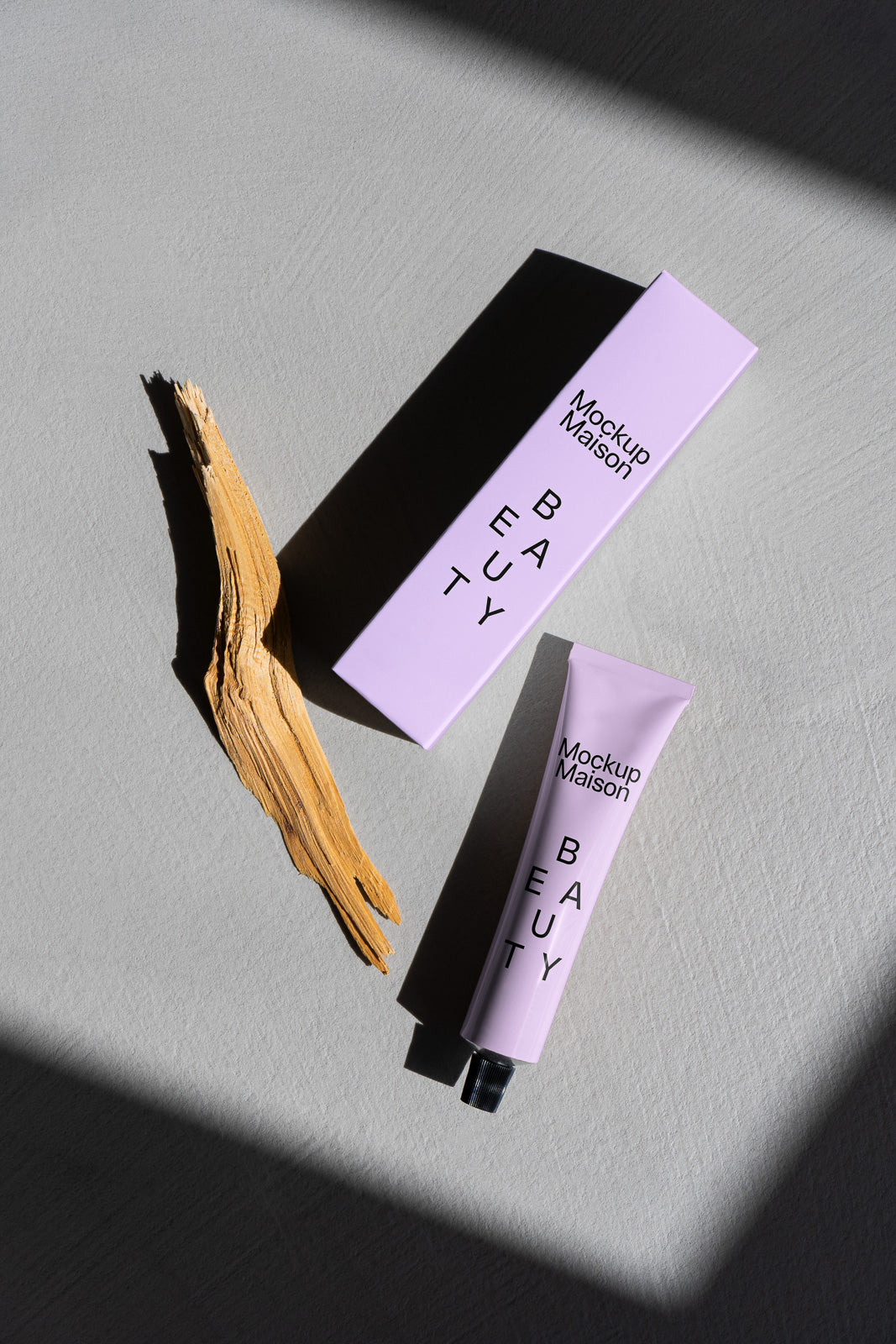 PSD mockup of a lavender beauty tube and box, labeled "Mockup Maison," placed on a textured surface next to a piece of wood under soft shadow.