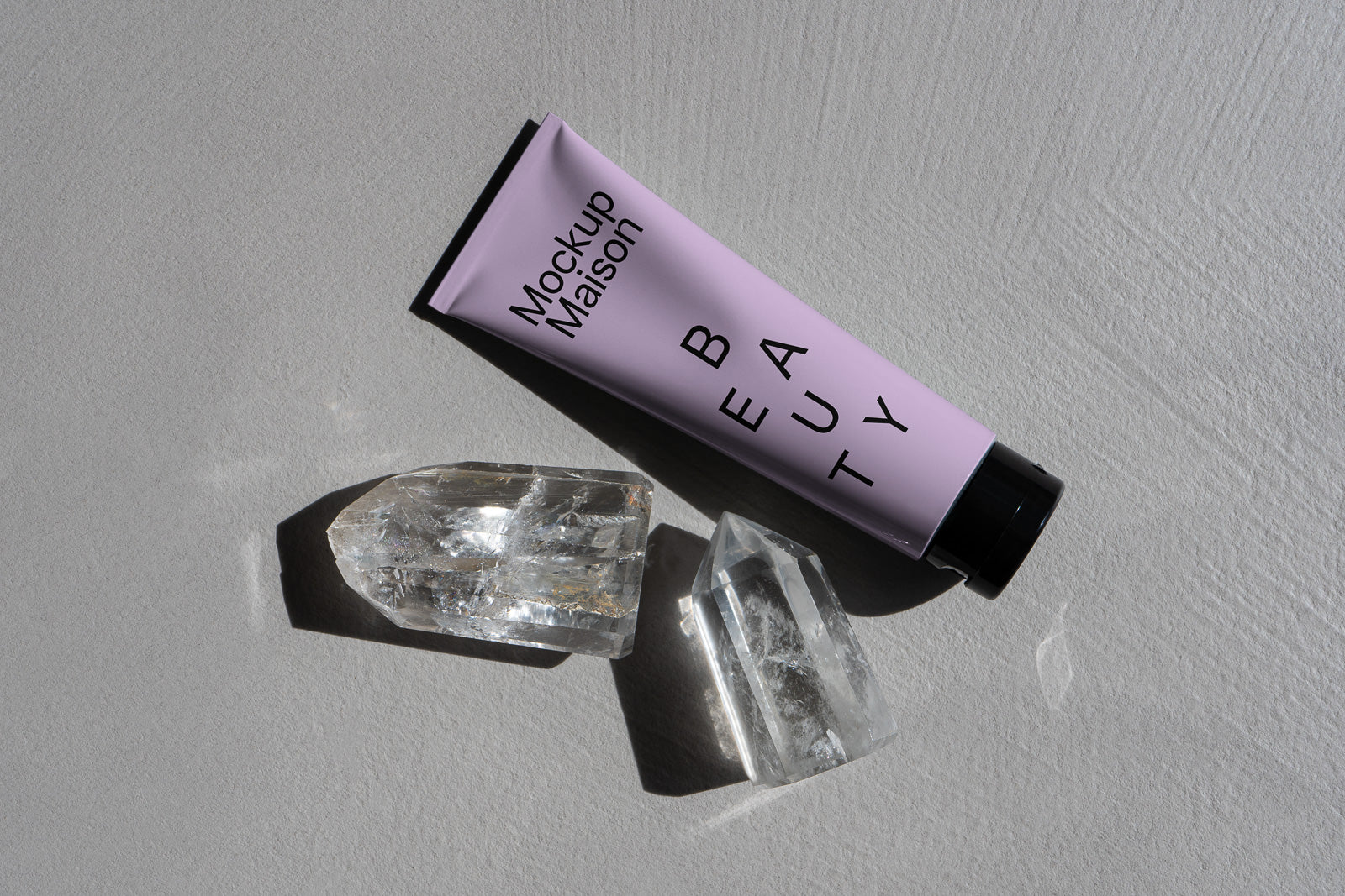 PSD mockup of a lavender-colored beauty tube labeled "Mockup Maison" with crystals on a textured gray surface.