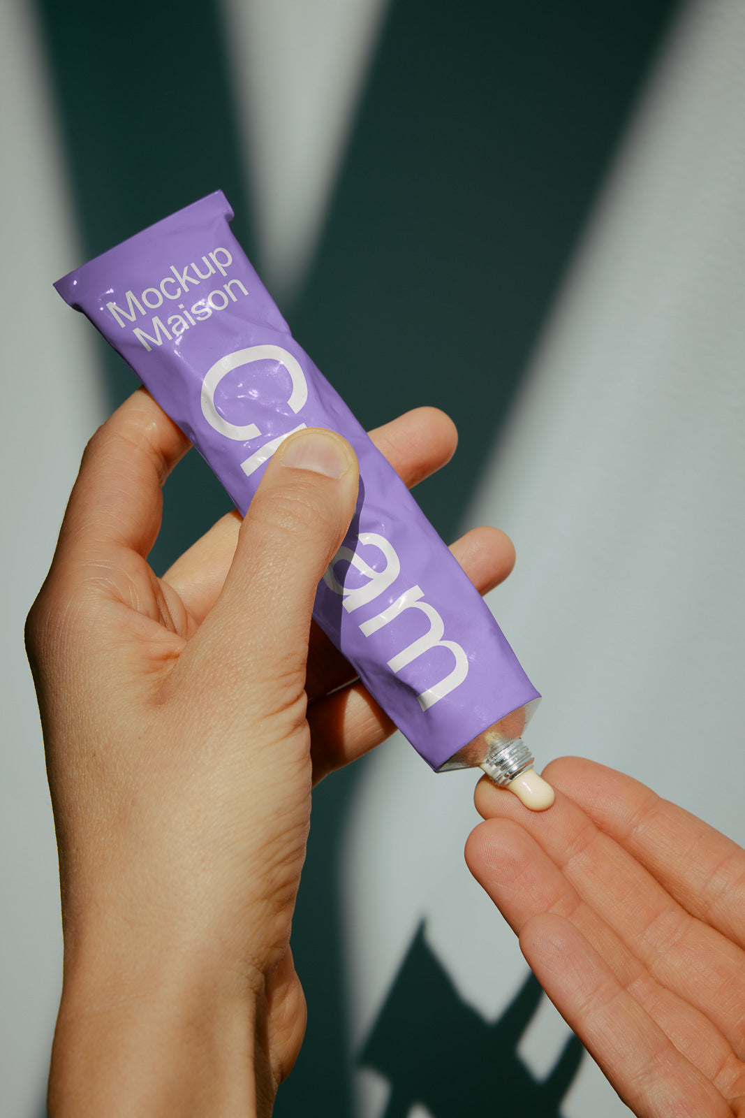 PSD mockup of a person holding a purple cream tube labeled "Mockup Maison" with cream being squeezed onto their fingertip.