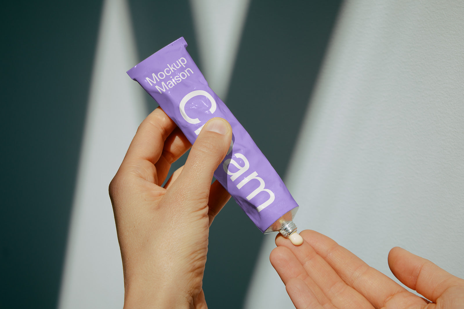 PSD mockup of a hand squeezing cream from a purple tube labeled "Mockup Maison" onto fingertips, set against a softly lit background.
