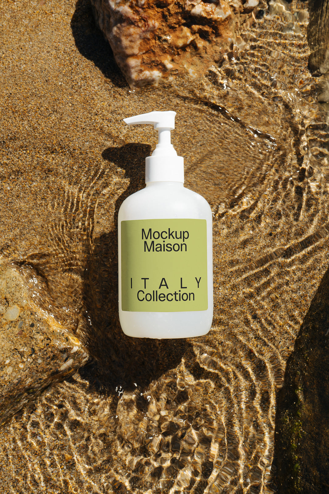 PSD mockup of a white pump bottle labeled "Mockup Maison ITALY Collection," set on a wet sandy surface with rippling water.