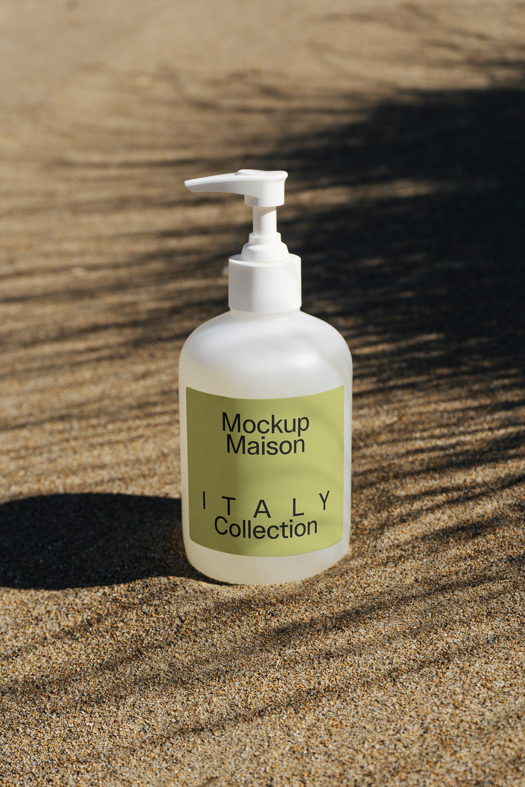 PSD mockup of a white pump bottle labeled "Mockup Maison Italy Collection," placed on sand with shadows cast on the surface.
