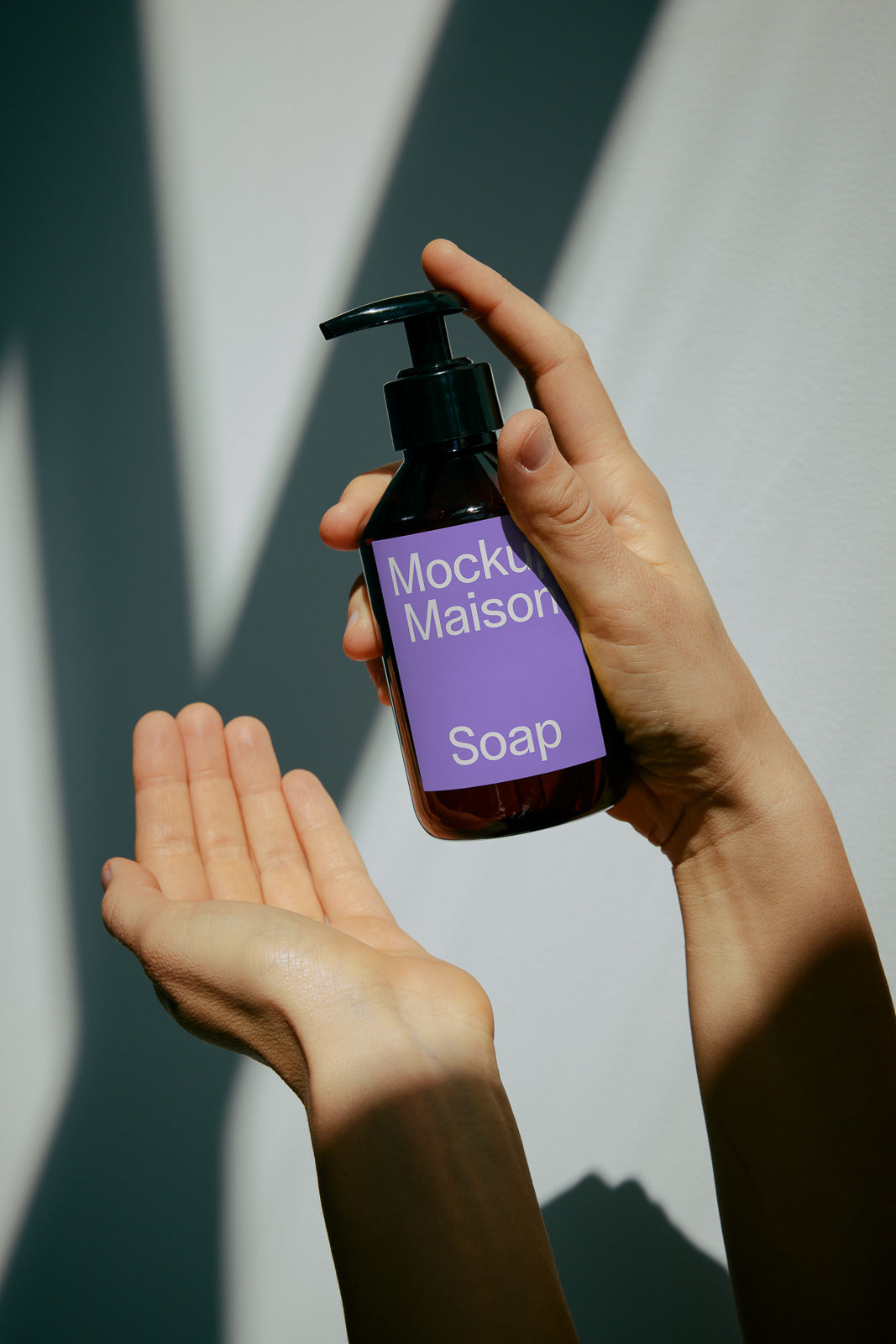 PSD mockup of a liquid soap bottle labeled "Mockup Maison" held above an open hand under dramatic lighting and shadows.