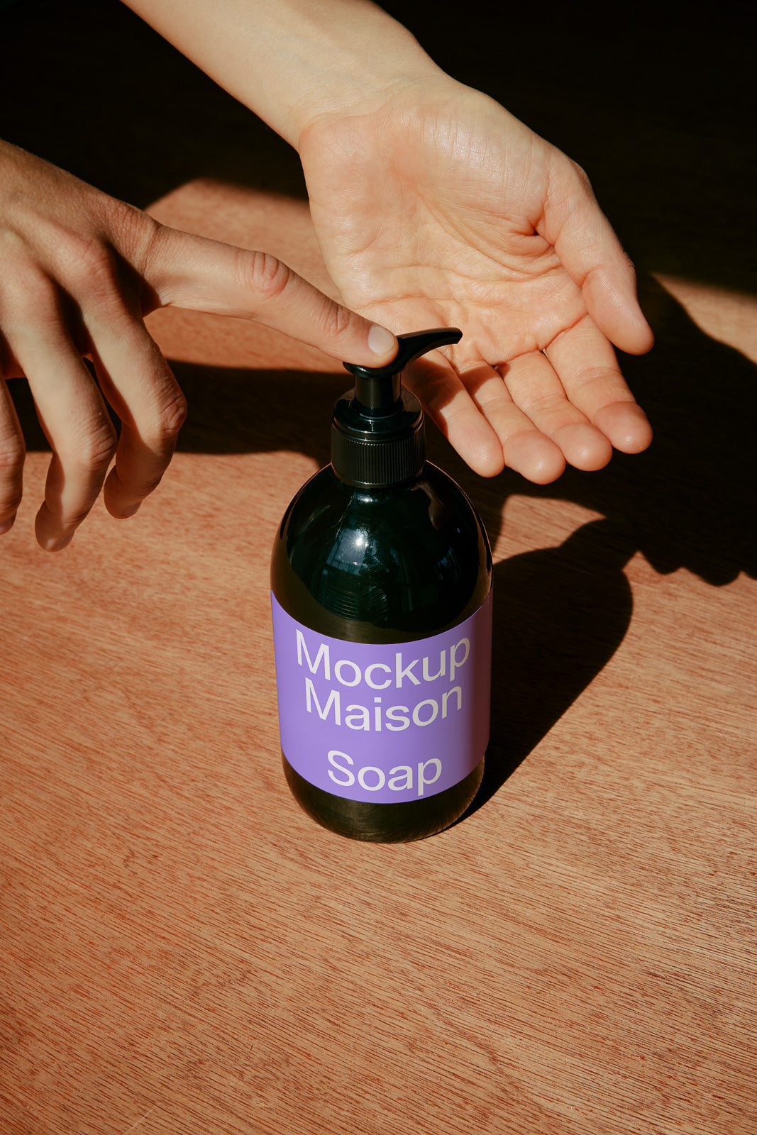 PSD mockup of a soap bottle with a purple label being used as liquid is dispensed onto an open hand, set on a wooden surface.