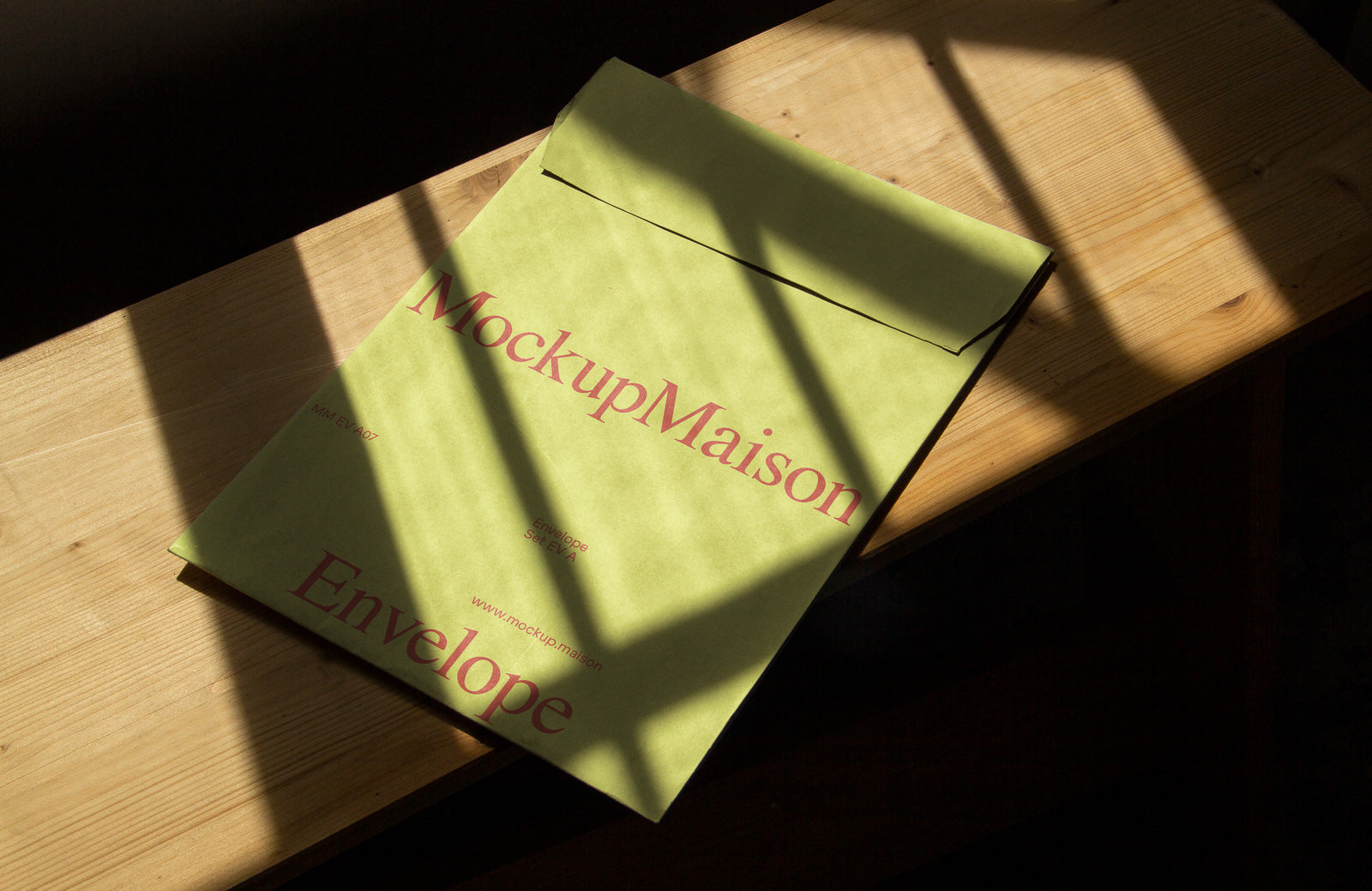 PSD mockup of a green envelope labeled "MockupMaison" placed on a wooden surface with shadows from window blinds.