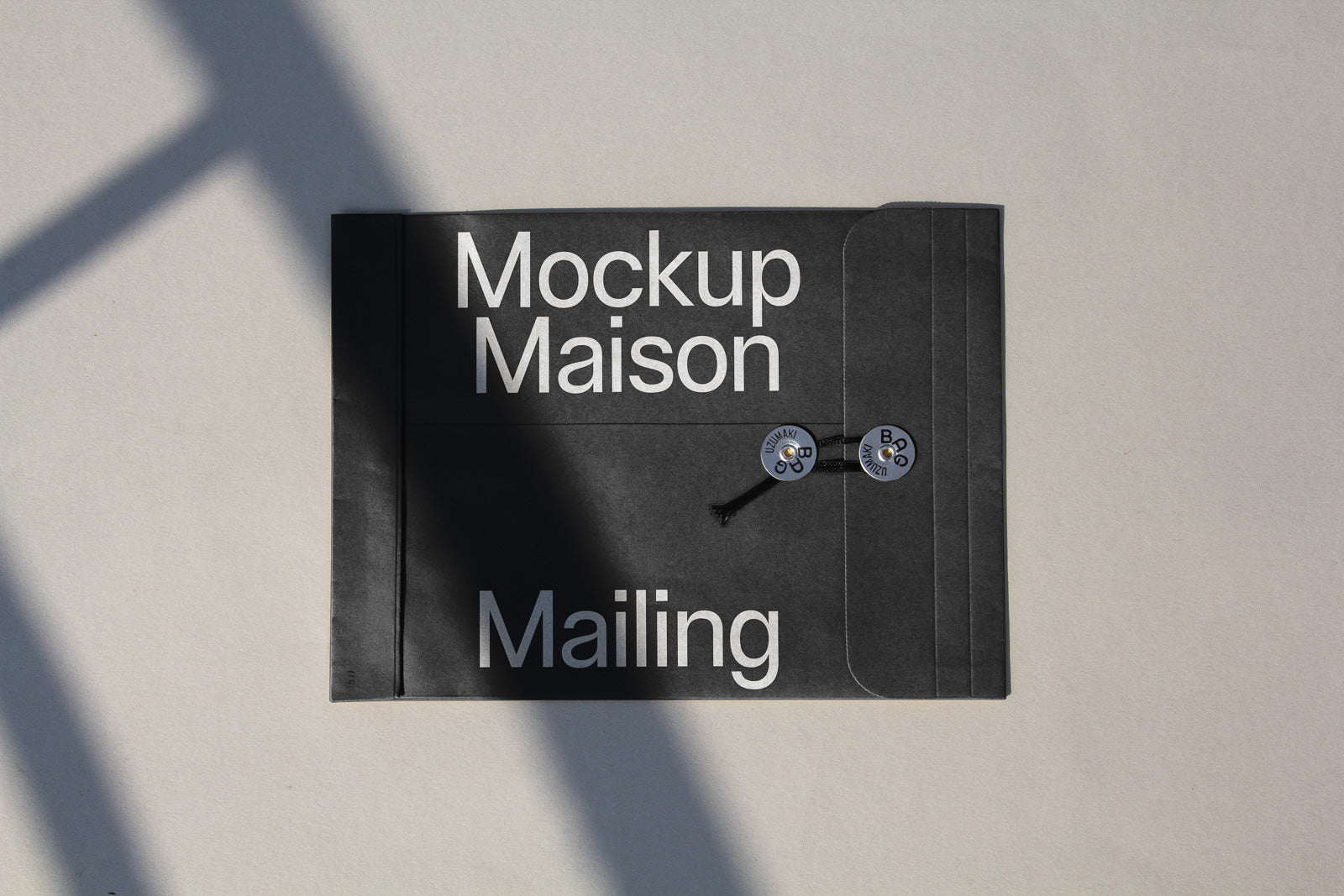 PSD mockup of a black envelope with "Mockup Maison Mailing" in bold white letters, featuring two round string fasteners.