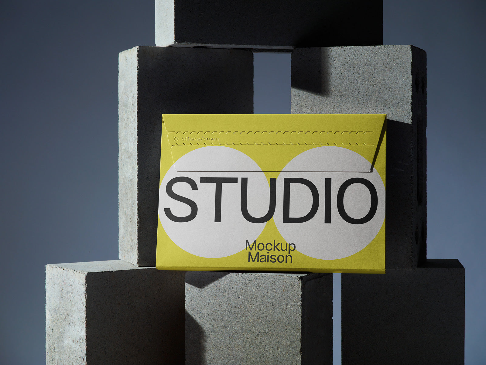 PSD mockup of a yellow envelope labeled "STUDIO Mockup Maison," resting against stacked concrete blocks, highlighting its design elements and structure.