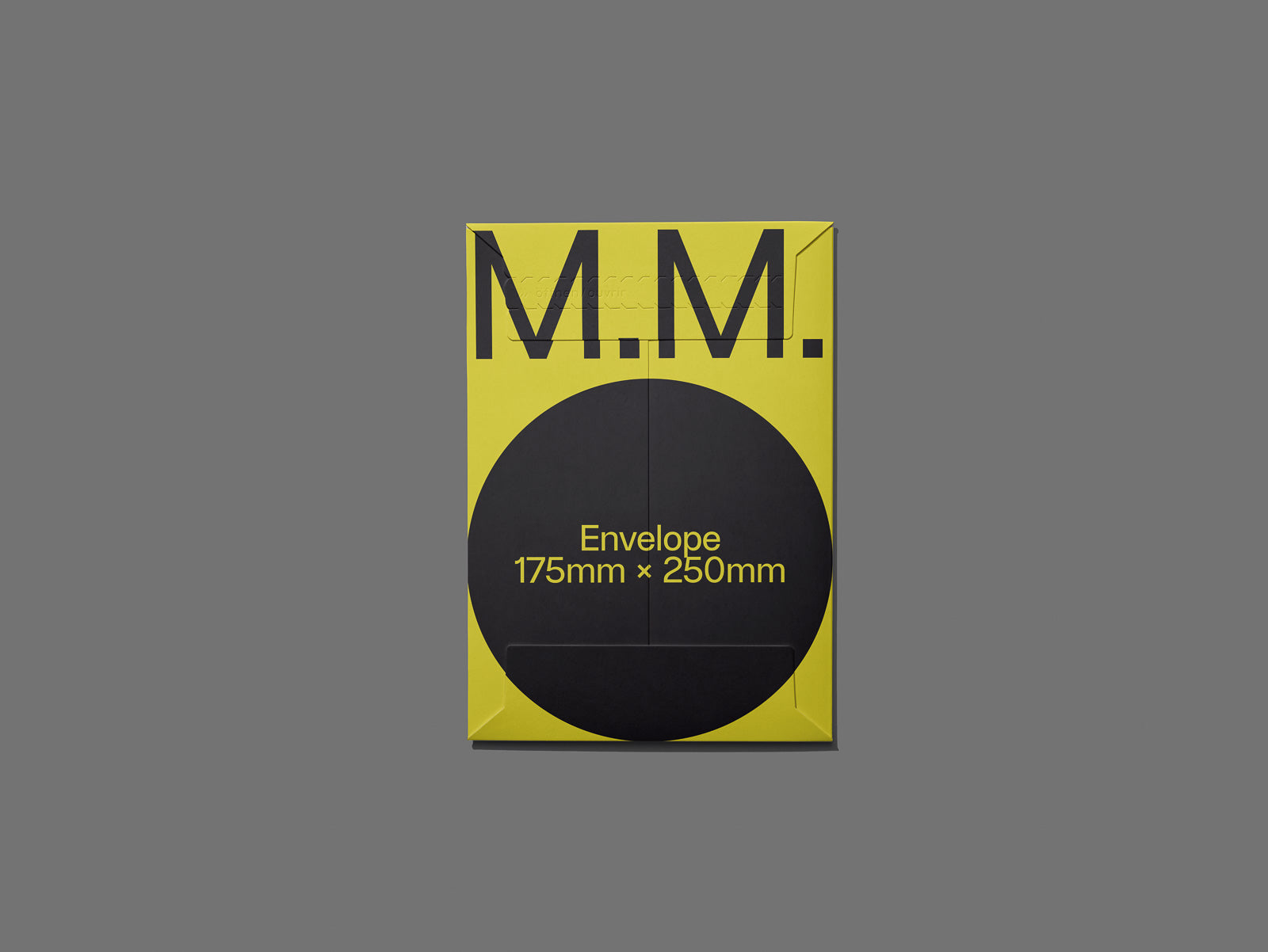 PSD mockup of a yellow envelope labeled "M.M. Envelope 175mm × 250mm" with a black circle design on a gray background.