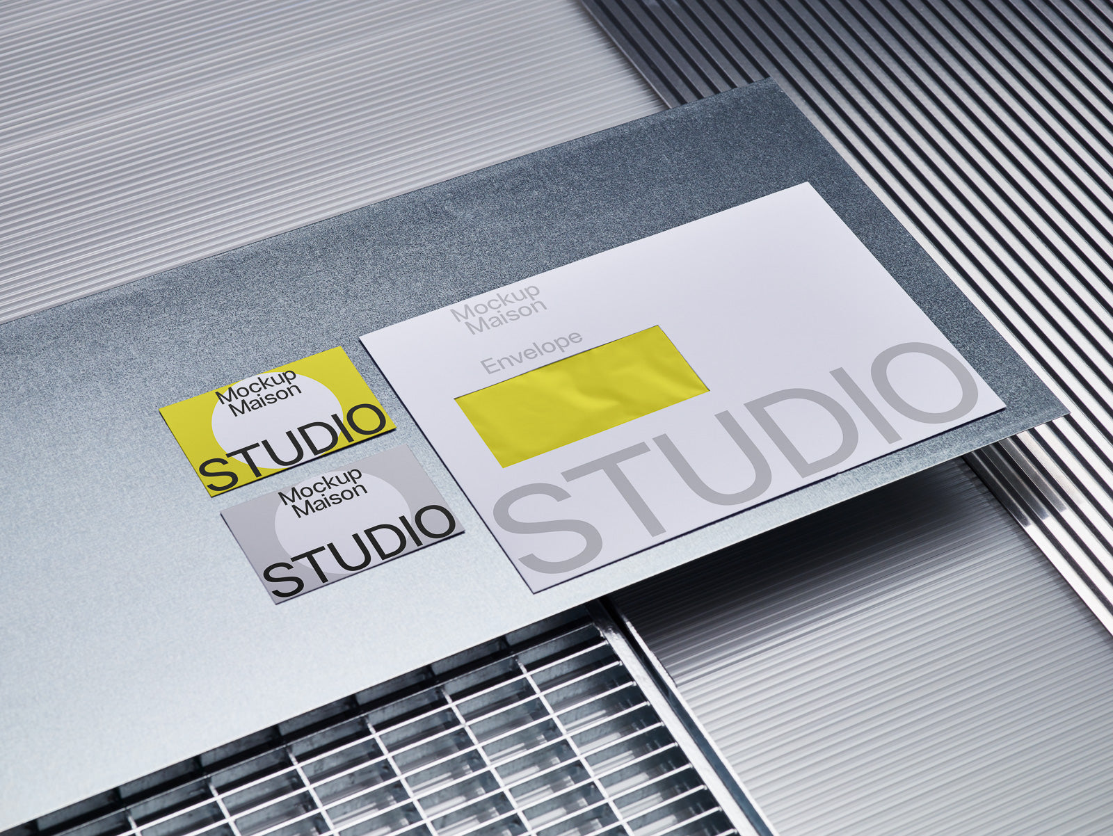 PSD mockup of two studio business cards and an envelope on a metallic, textured surface with industrial elements.