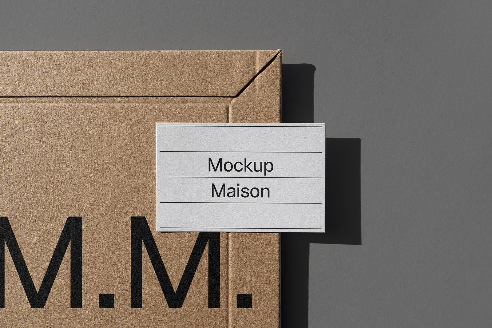 PSD mockup of a cardboard package with the text "Mockup Maison" on a white card, placed on a gray background.