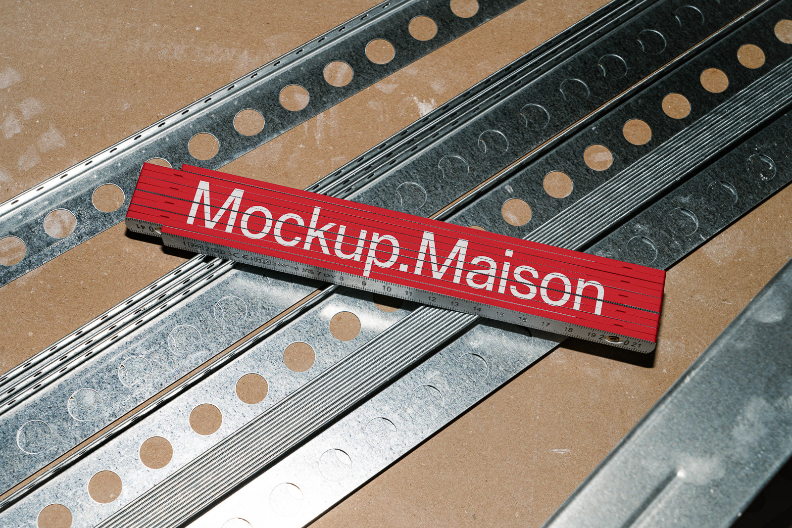 PSD mockup of a red folding ruler with "Mockup. Maison" text, placed on metal strips over a wooden surface, in a well-lit environment.