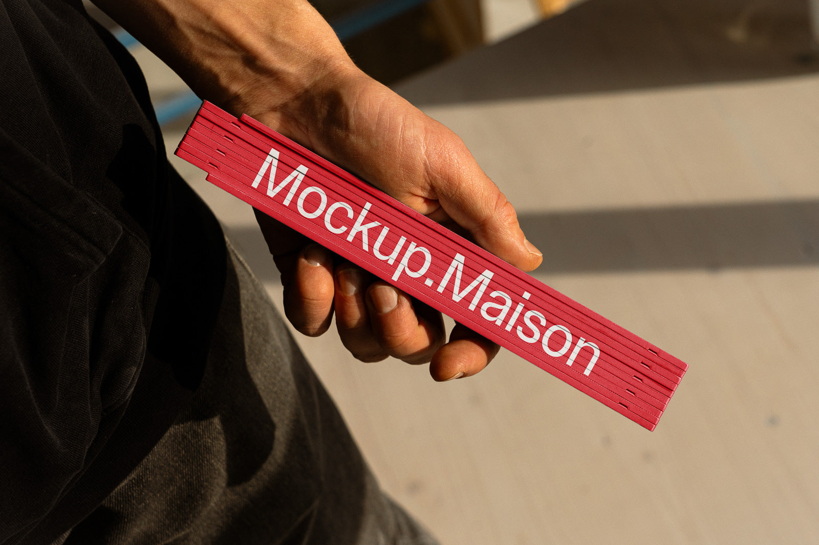 PSD mockup of a person holding a red folding ruler labeled "Mockup.Maison" against a light background, casting a shadow.