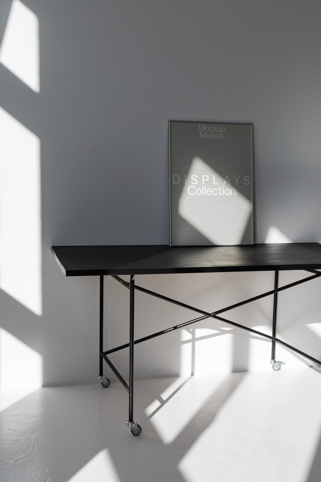PSD mockup of a minimalistic poster resting on a dark wooden table with metal legs and caster wheels, set against a wall with geometric shadows.