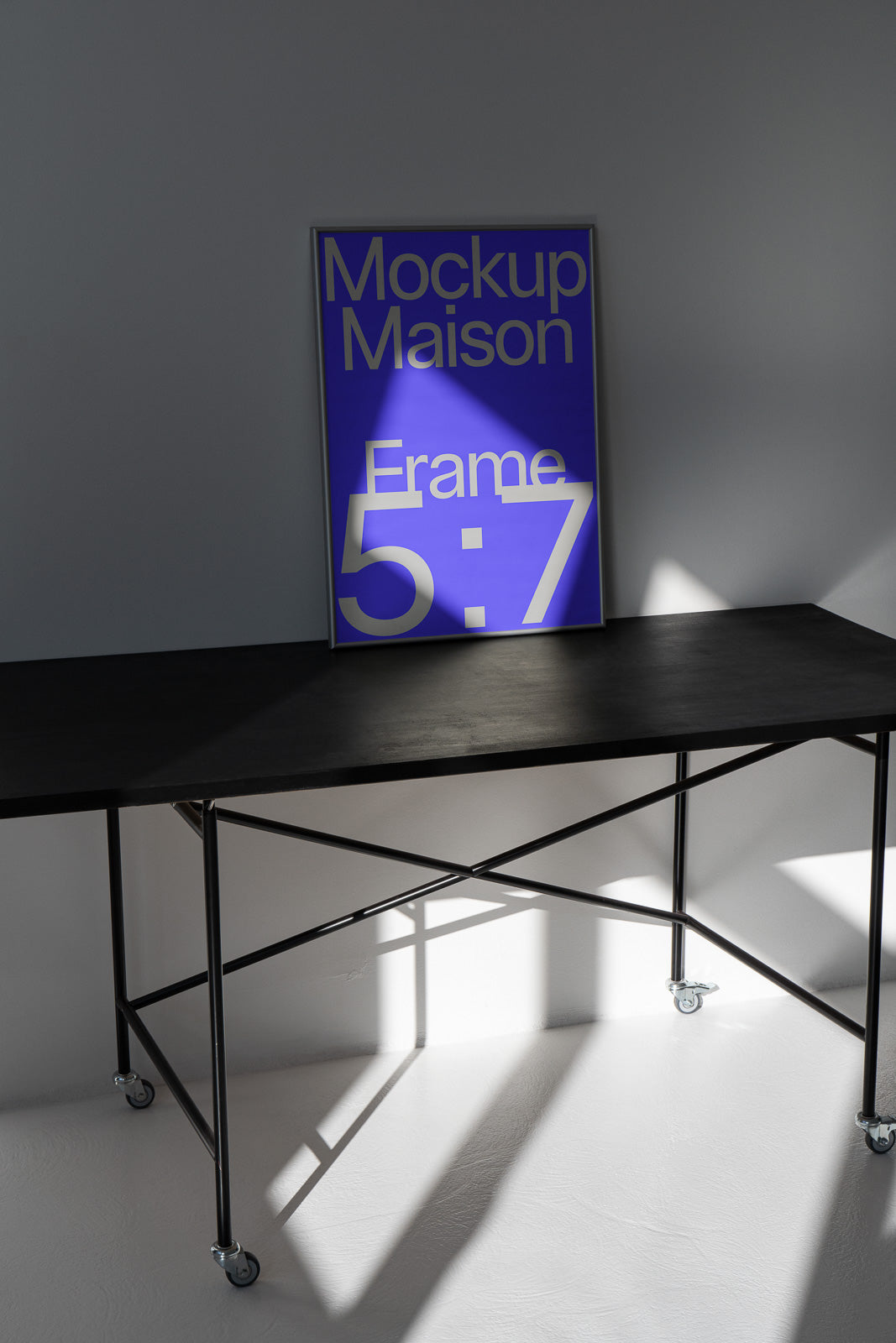 PSD mockup of a 5:7 poster leaning against a wall on a dark metal table with wheels, illuminated by natural light casting geometric shadows.