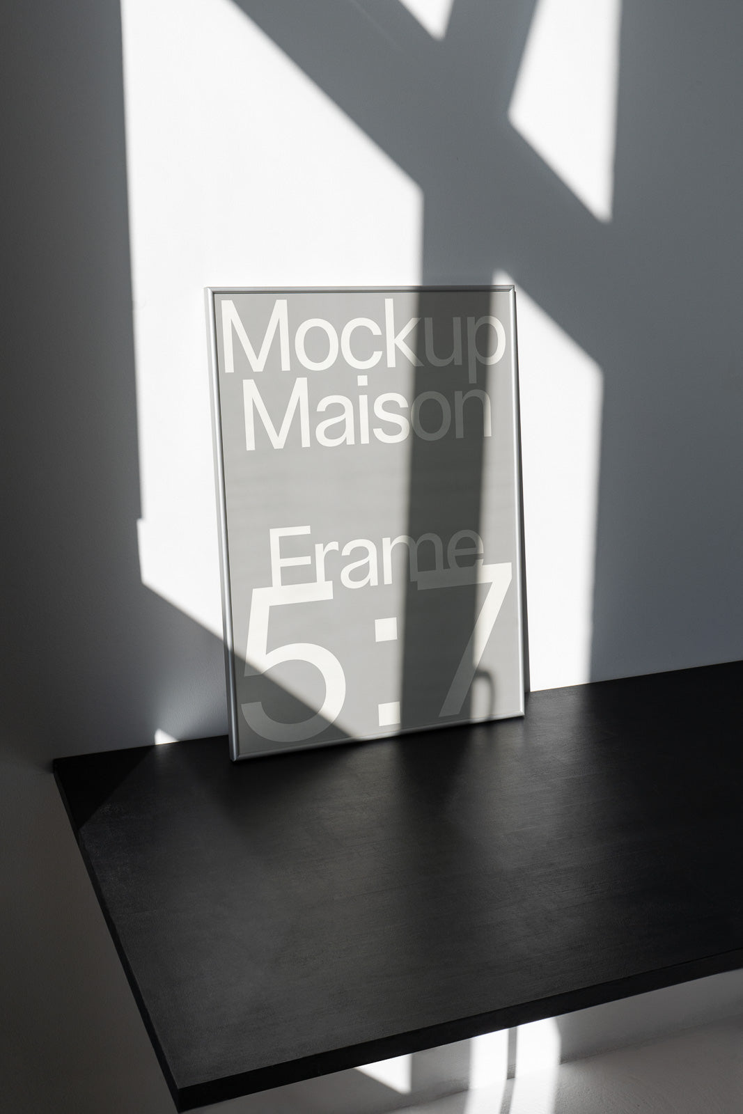 PSD mockup of a vertical 5x7 frame labeled "Mockup Maison" resting on a dark surface with soft shadows on a white wall behind it.