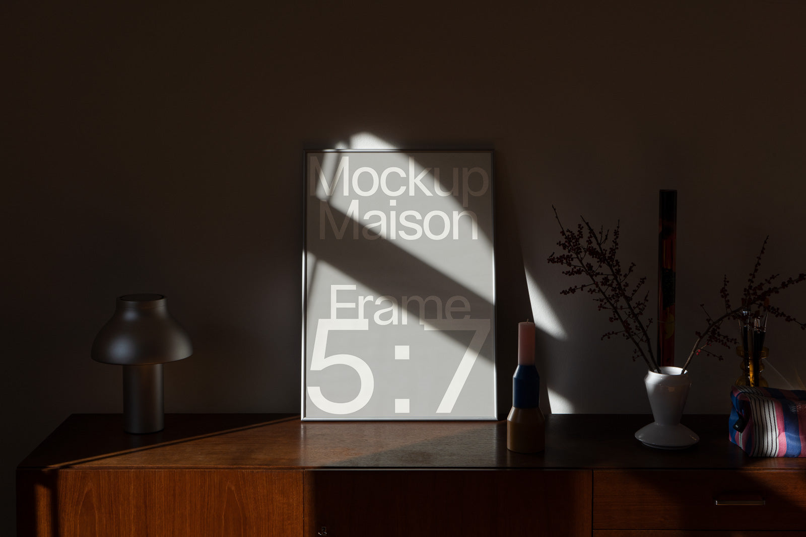 PSD mockup of a 5x7 frame on a wooden shelf beside a modern lamp and decorative objects in warm ambient lighting.
