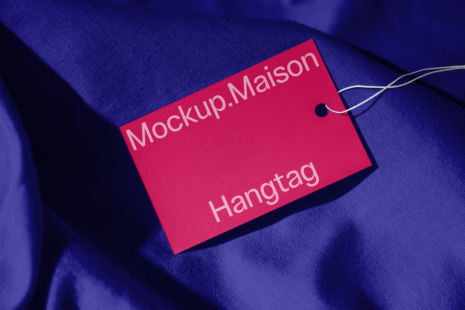 PSD mockup of a red hangtag with "Mockup.Maison Hangtag" text, attached with a string on blue fabric background.