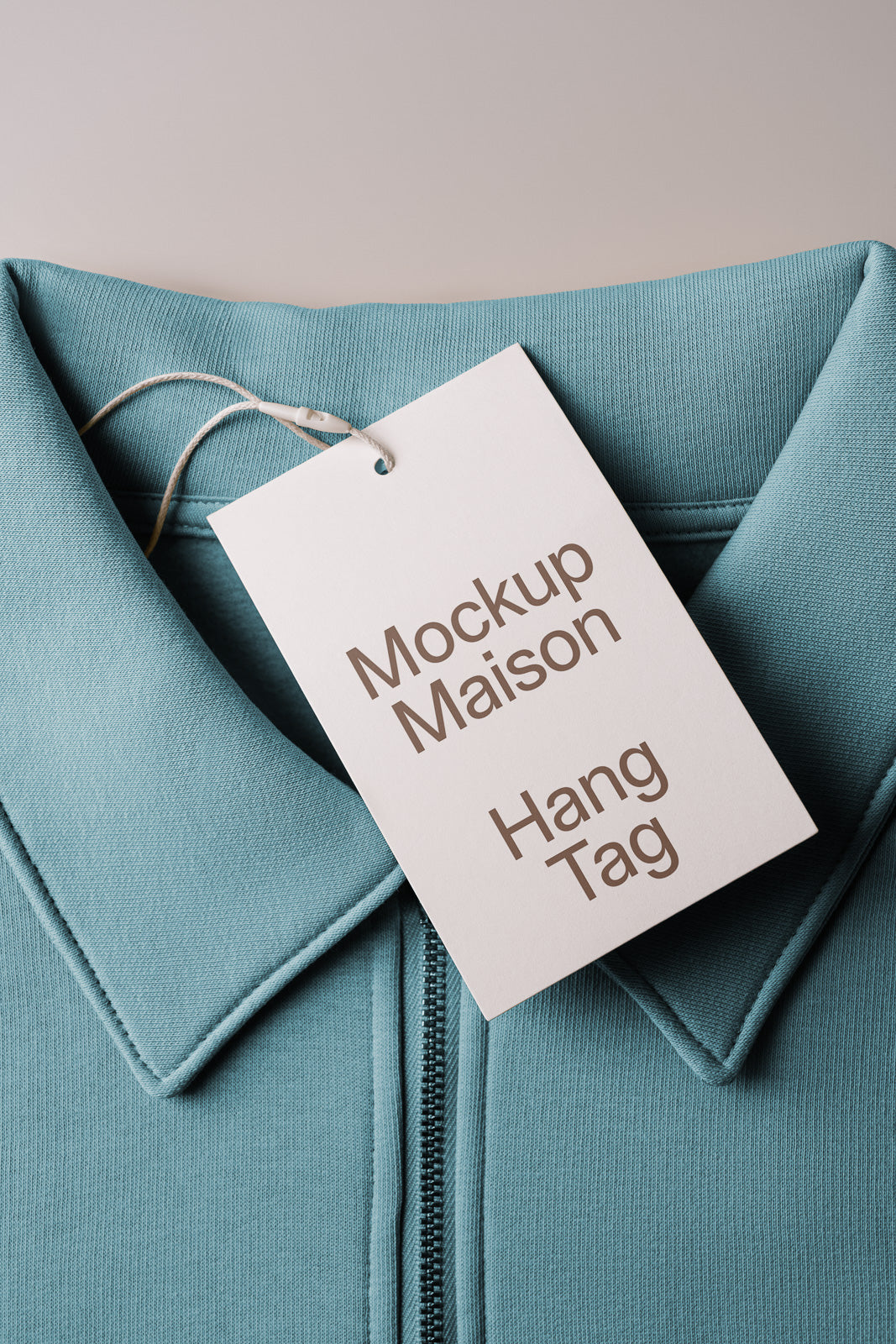 PSD mockup of a teal garment with a white tag labeled "Mockup Maison Hang Tag," highlighting fabric texture and tag design.