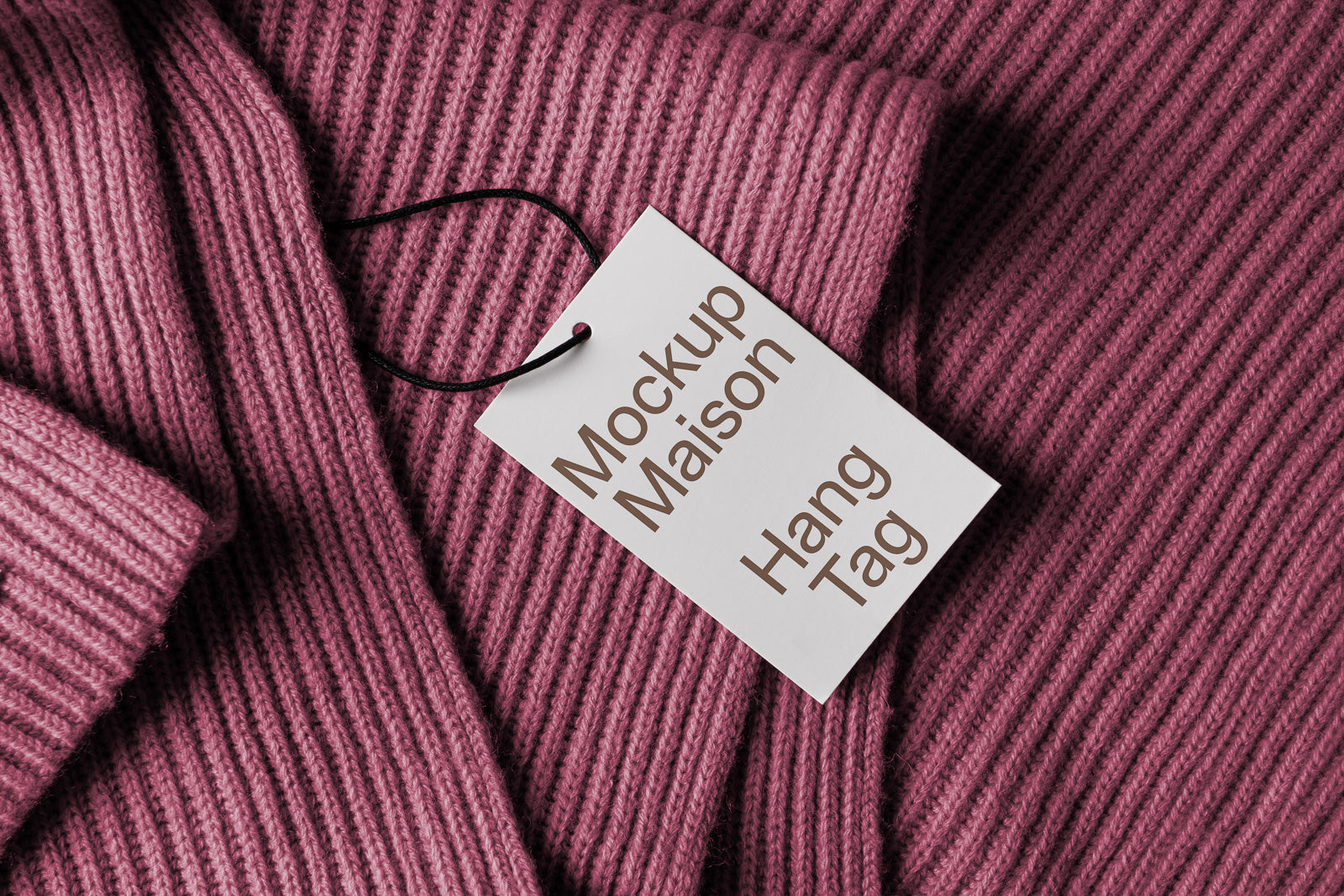 PSD mockup of a cardboard hang tag with "Mockup Maison Hang Tag" text, attached to a pink ribbed fabric garment, featuring a black string.