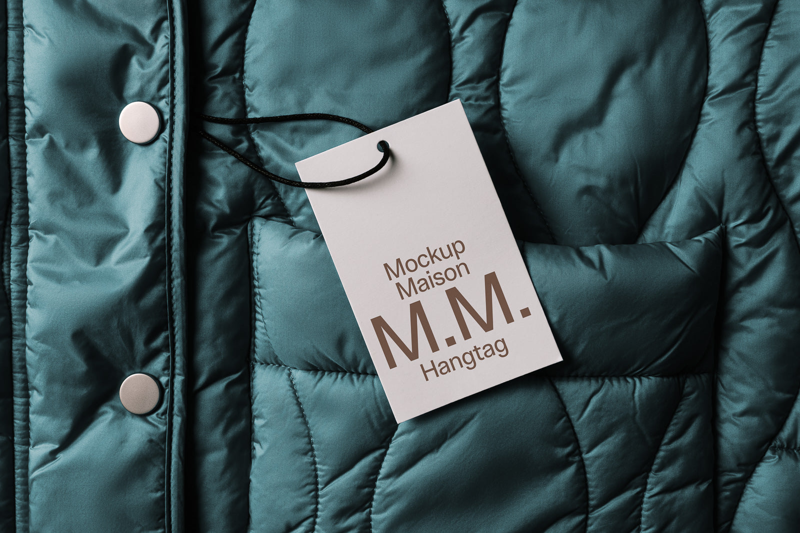 PSD mockup of a quilted jacket in teal with a cardboard hangtag labeled "Mockup Maison M.M. Hangtag." The tag is attached with a thin black string.