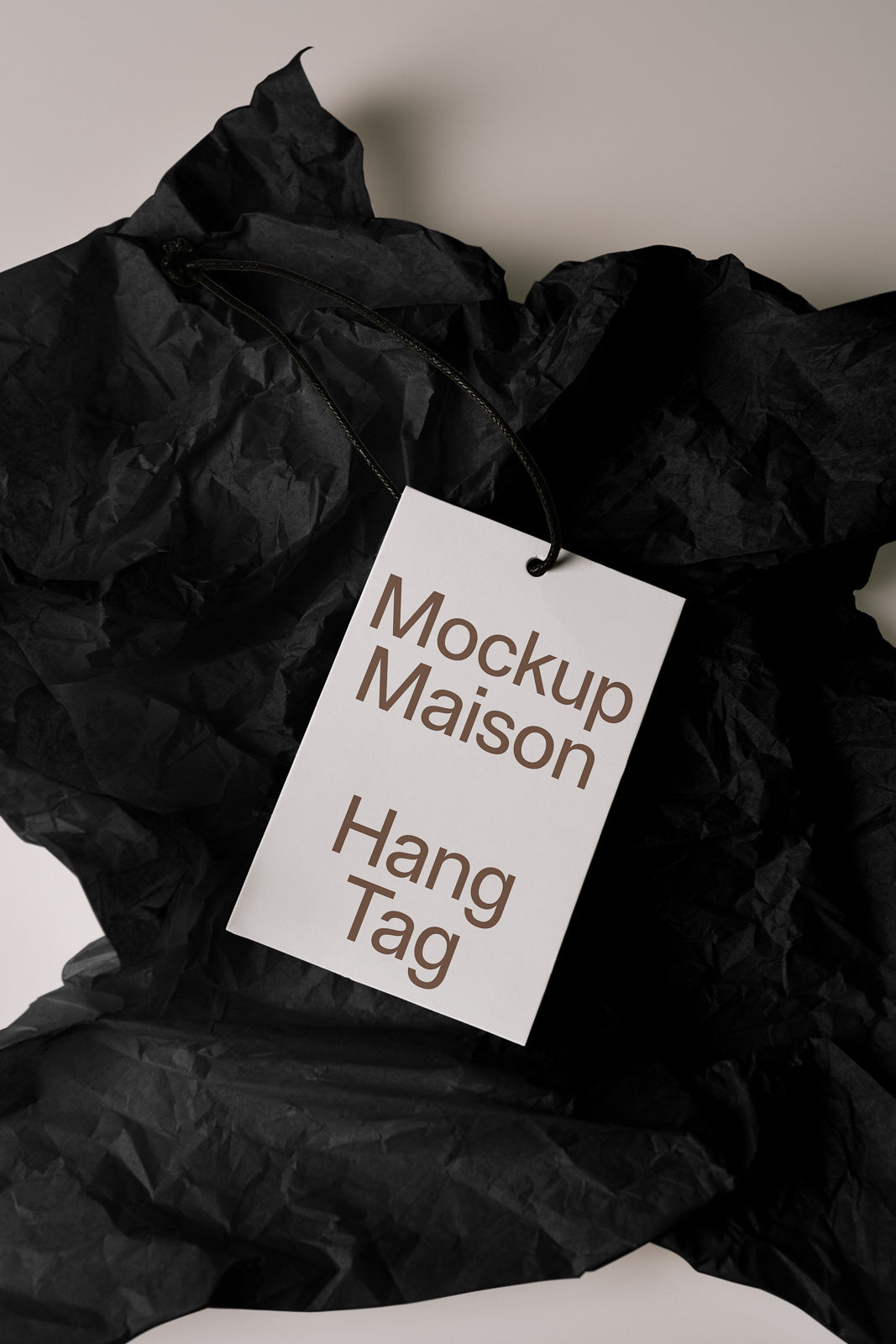 PSD mockup of a rectangular hang tag with black string on crumpled black tissue paper, featuring text "Mockup Maison Hang Tag".