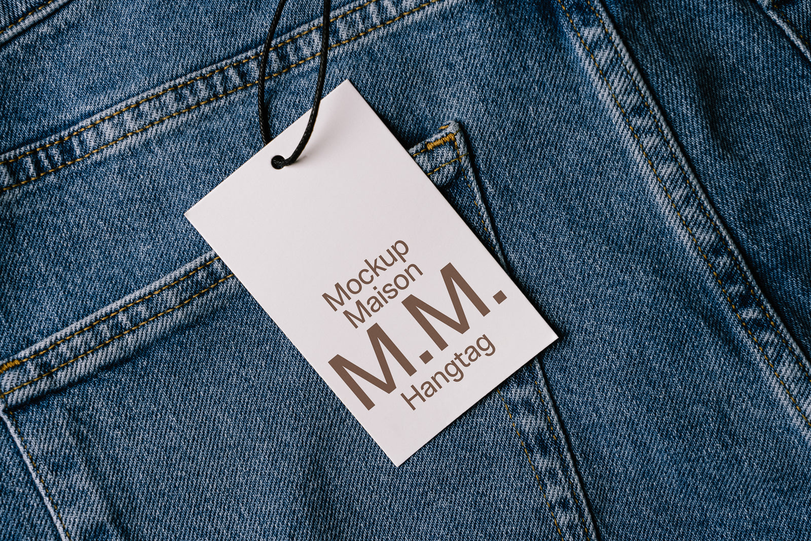 PSD mockup of a hangtag with "M.M." branding attached to denim jeans, showcasing label design and texture.