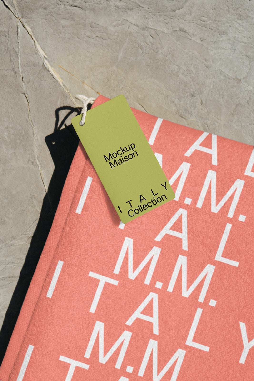 PSD mockup of a salmon-colored fabric with white text and a green tag labeled "Mockup Maison" and "ITALY Collection" attached with string.