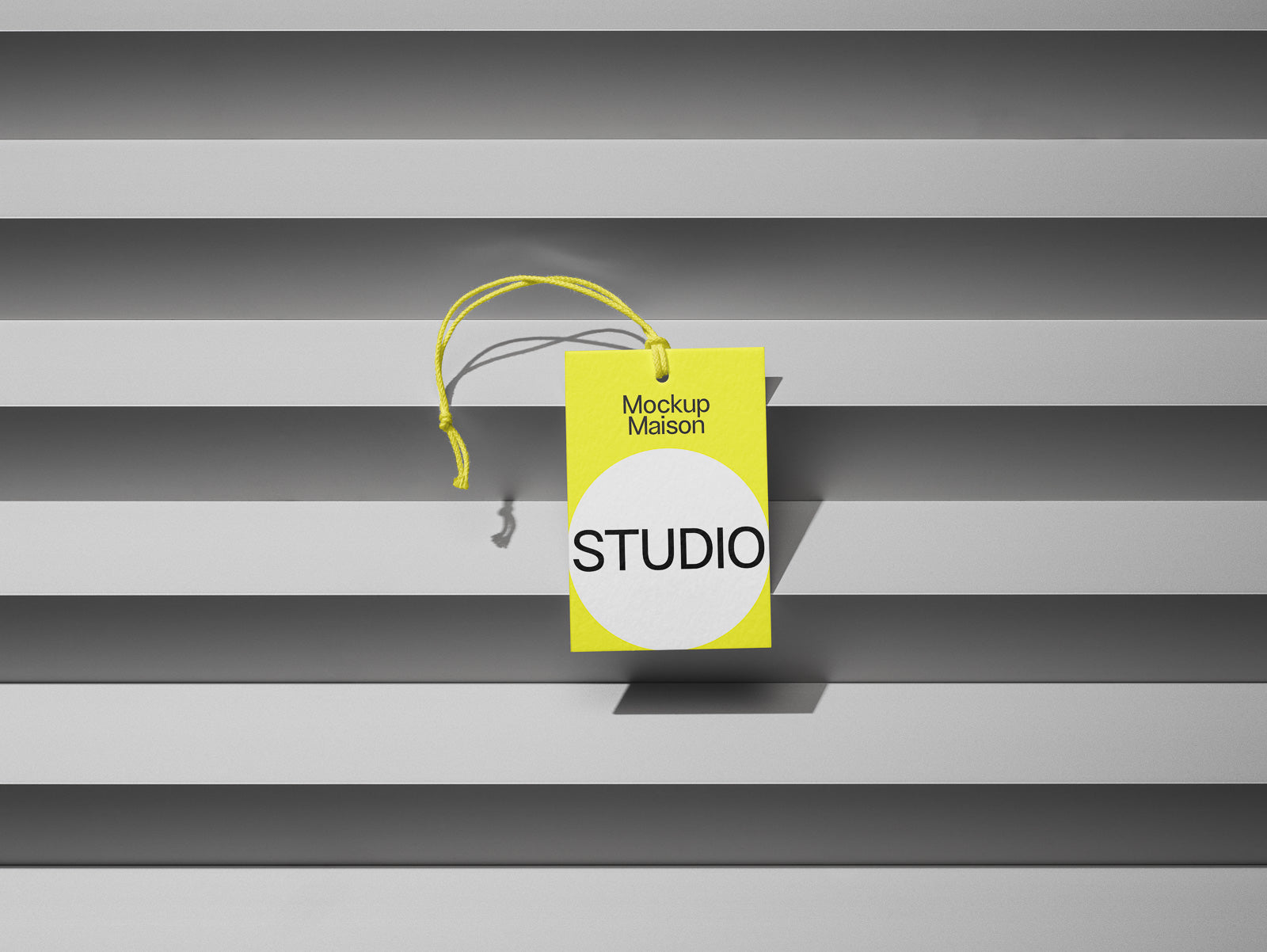 PSD mockup of a bright yellow tag with "Mockup Maison" and "STUDIO" text, hanging on a series of horizontal grey panels casting shadows.