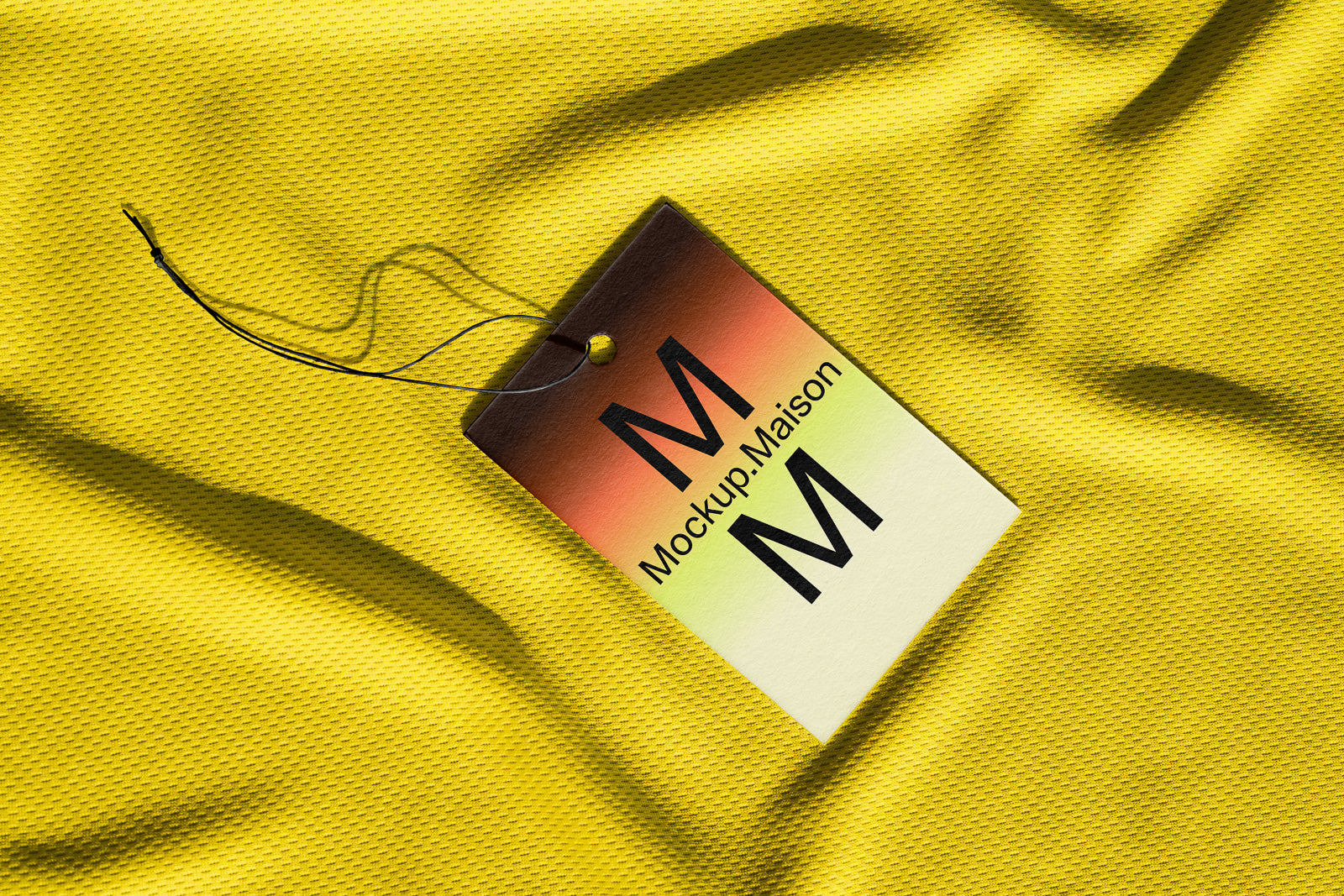 PSD mockup of a clothing tag with "Mockup.Maison" printed, set on a textured yellow fabric background.