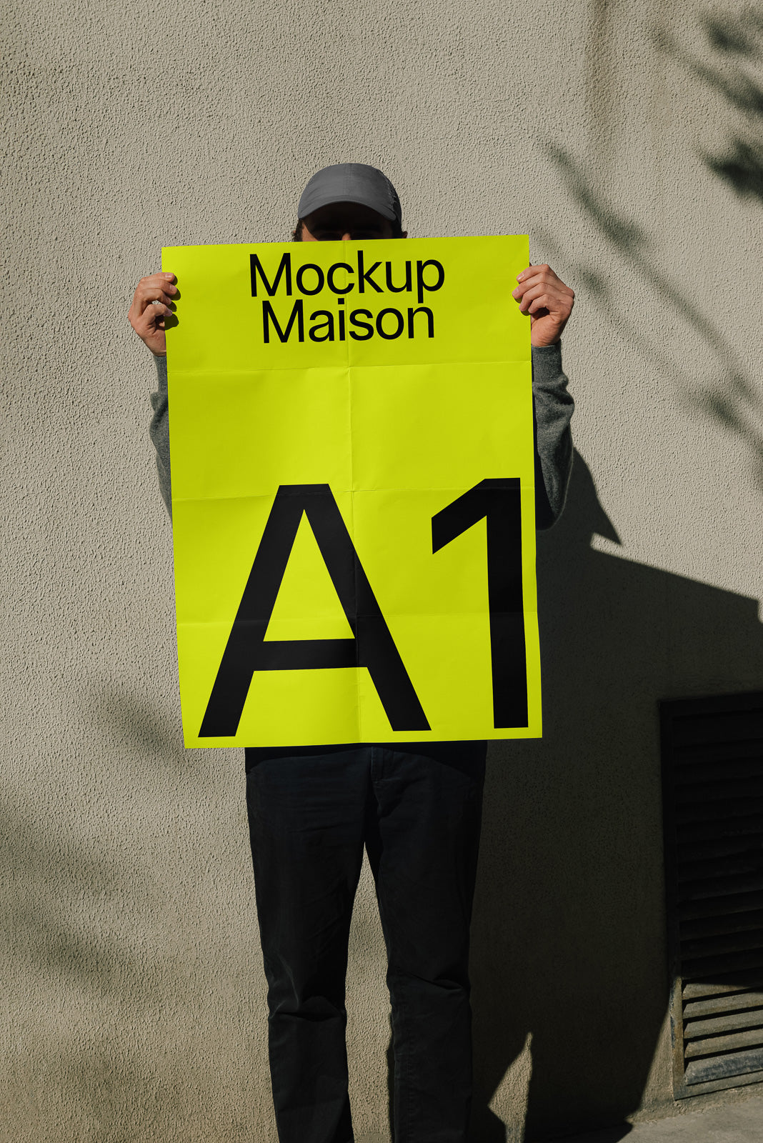 PSD mockup of a person holding a bright yellow A1 poster against a textured wall, partially covering their face and wearing dark pants.
