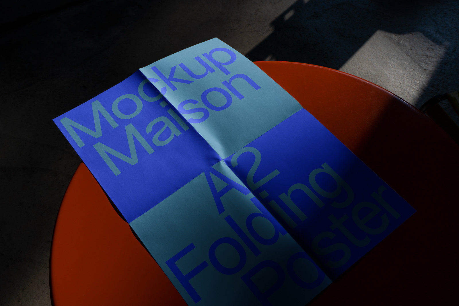PSD mockup of an A2 folding poster with bold text, placed on an orange table, partially in shadow, showcasing the design's layout and color scheme.