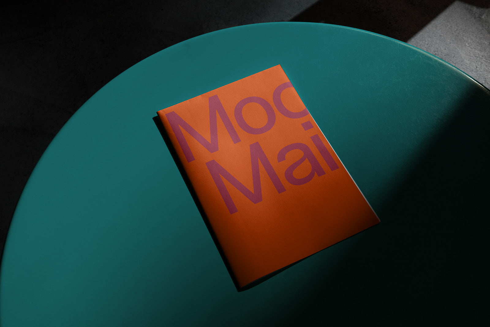 PSD mockup of an orange booklet with bold purple text on a teal round table, captured under dramatic lighting for emphasis.