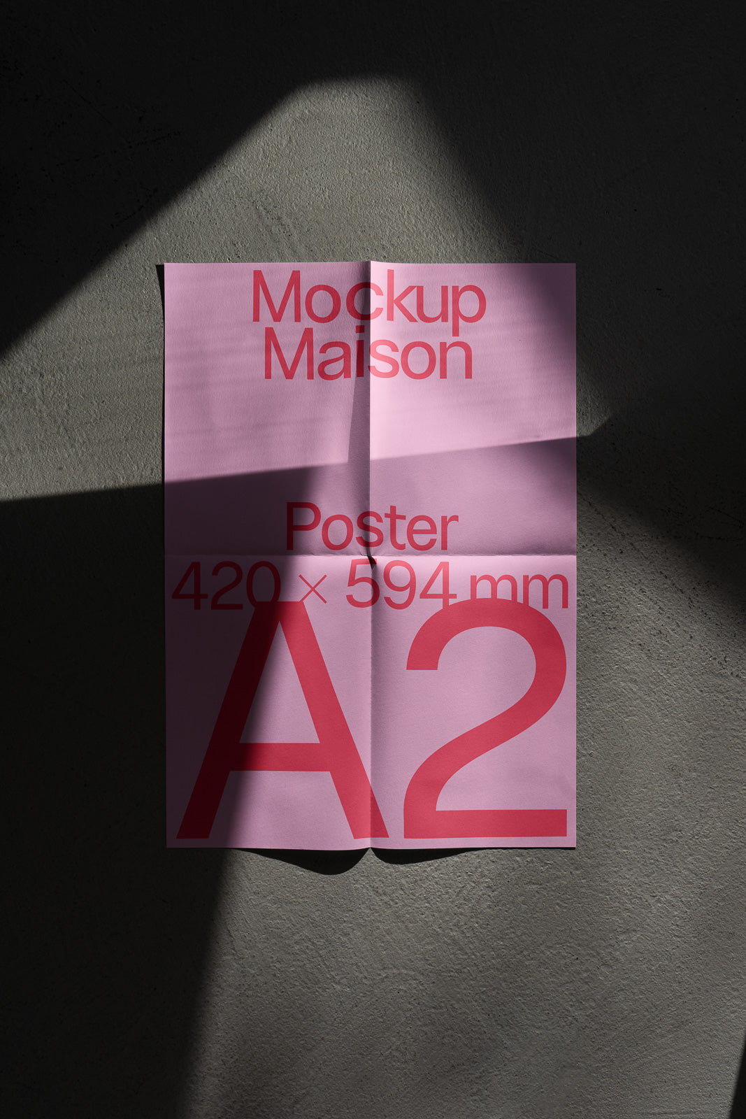 PSD mockup of a folded pink A2 poster with red text on a textured shadowed surface.