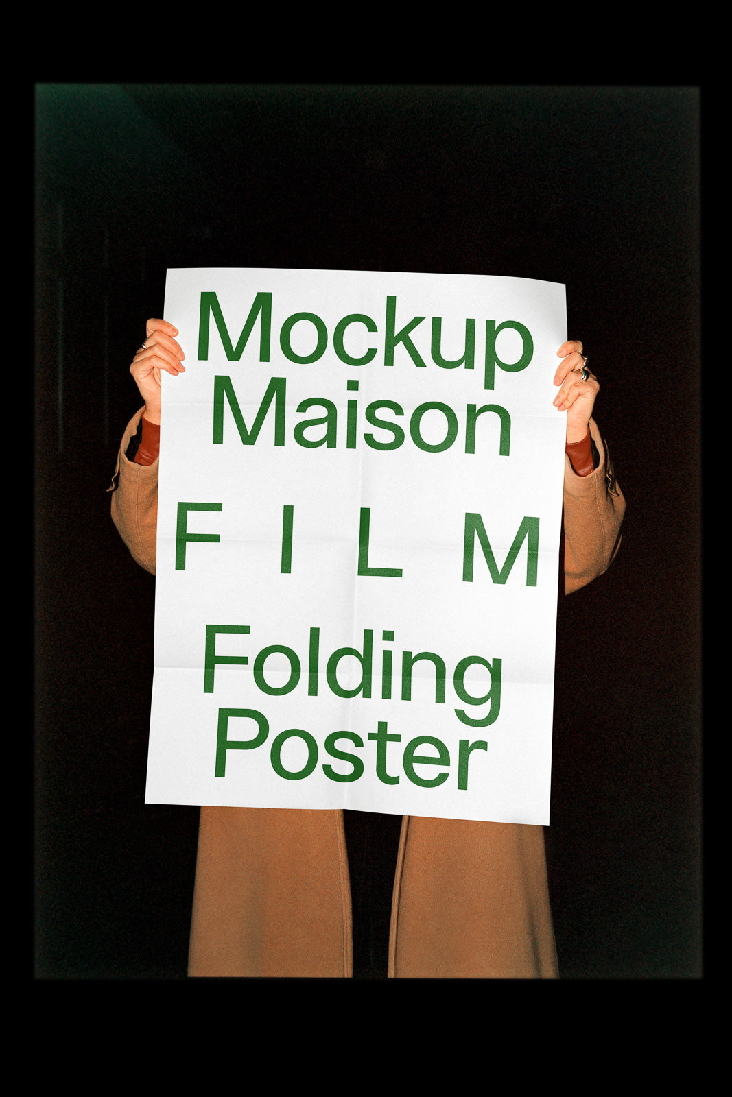 PSD mockup of a person holding a large folding poster with "Mockup Maison FILM Folding Poster" text printed in green, set against a dark background.