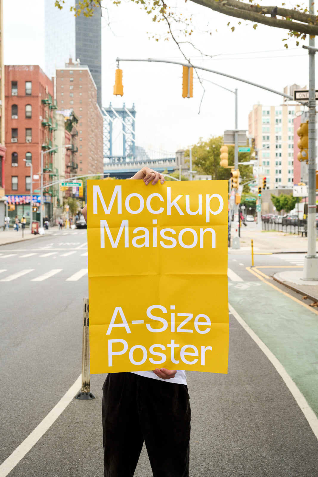 PSD mockup of a person holding a bright yellow poster with white text reading "Mockup Maison A-Size Poster" on an urban street backdrop.
