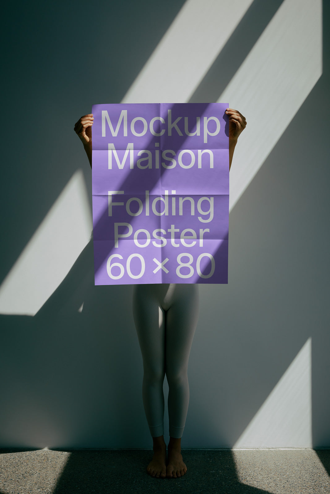 PSD mockup of a person holding a purple folding poster with the text "Mockup Maison Folding Poster 60 x 80" against a wall, lit by angled shadows.