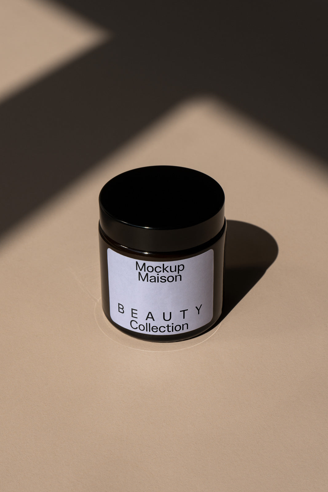 PSD mockup of a black jar labeled "Beauty Collection" placed on a beige surface with shadow patterns, featuring the text "Mockup Maison."