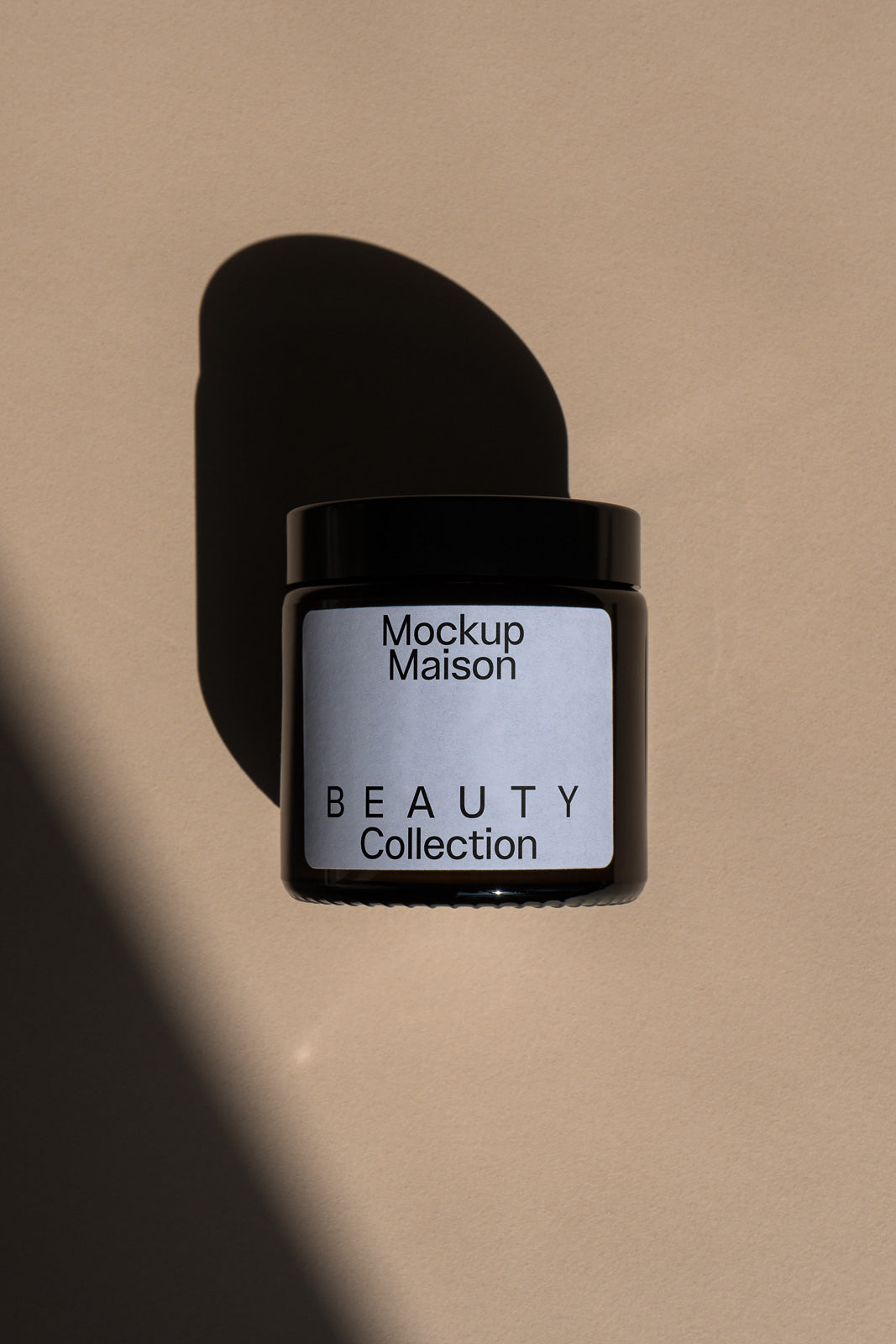 PSD mockup of a black jar labeled "Mockup Maison Beauty Collection" against a beige background with a shadow falling to the side.