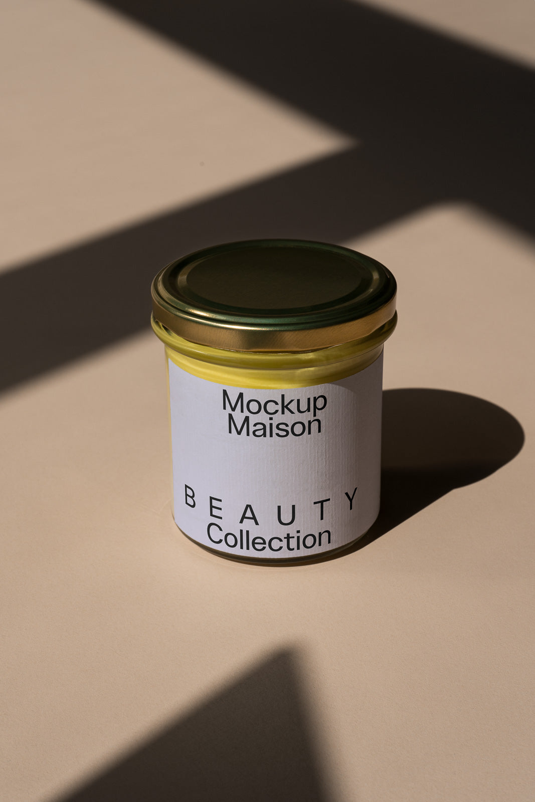 PSD mockup of a beauty product jar with a gold lid and labeled "Mockup Maison Beauty Collection" against a beige background with shadow effects.