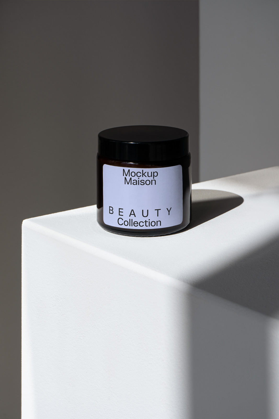 PSD mockup of a beauty collection jar labeled "Mockup Maison" placed on a white geometric surface, casting a shadow against a neutral background.