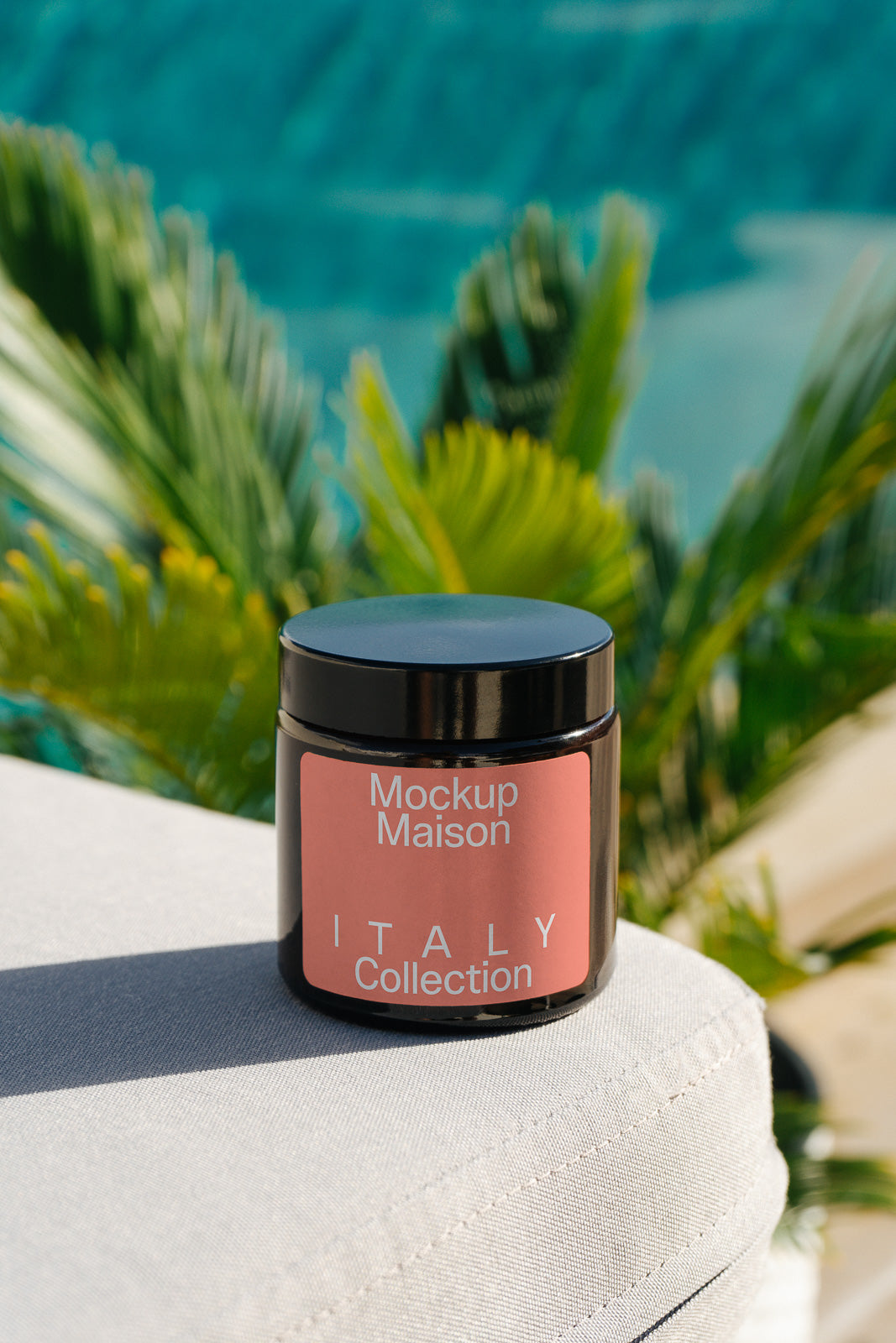 PSD mockup of a labeled jar from the Italy Collection on a fabric surface, with blurred tropical plants and water in the background.