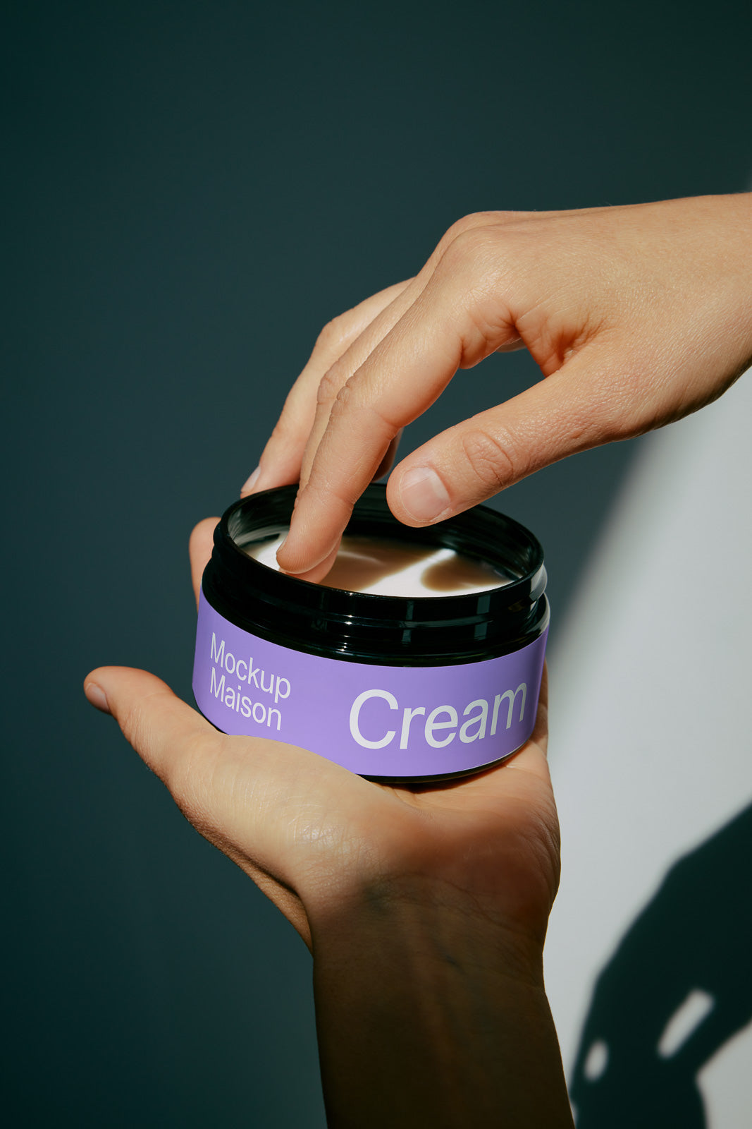 PSD mockup of a hand holding an open cream jar with a purple label titled "Mockup Maison" and "Cream," fingers dipping into the product.