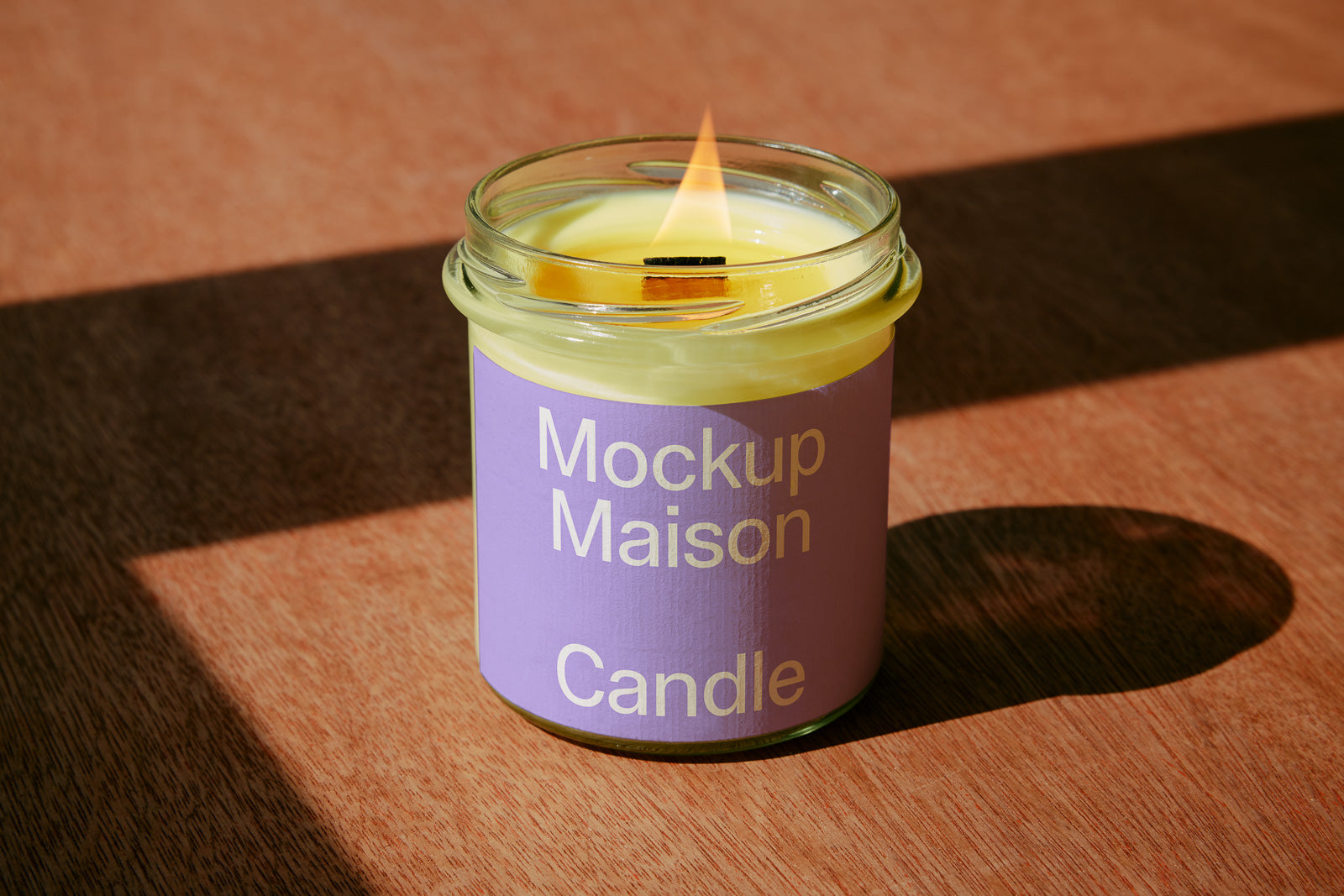 PSD mockup of a lit candle in a glass jar with a purple label reading "Mockup Maison Candle," placed on a wooden surface.