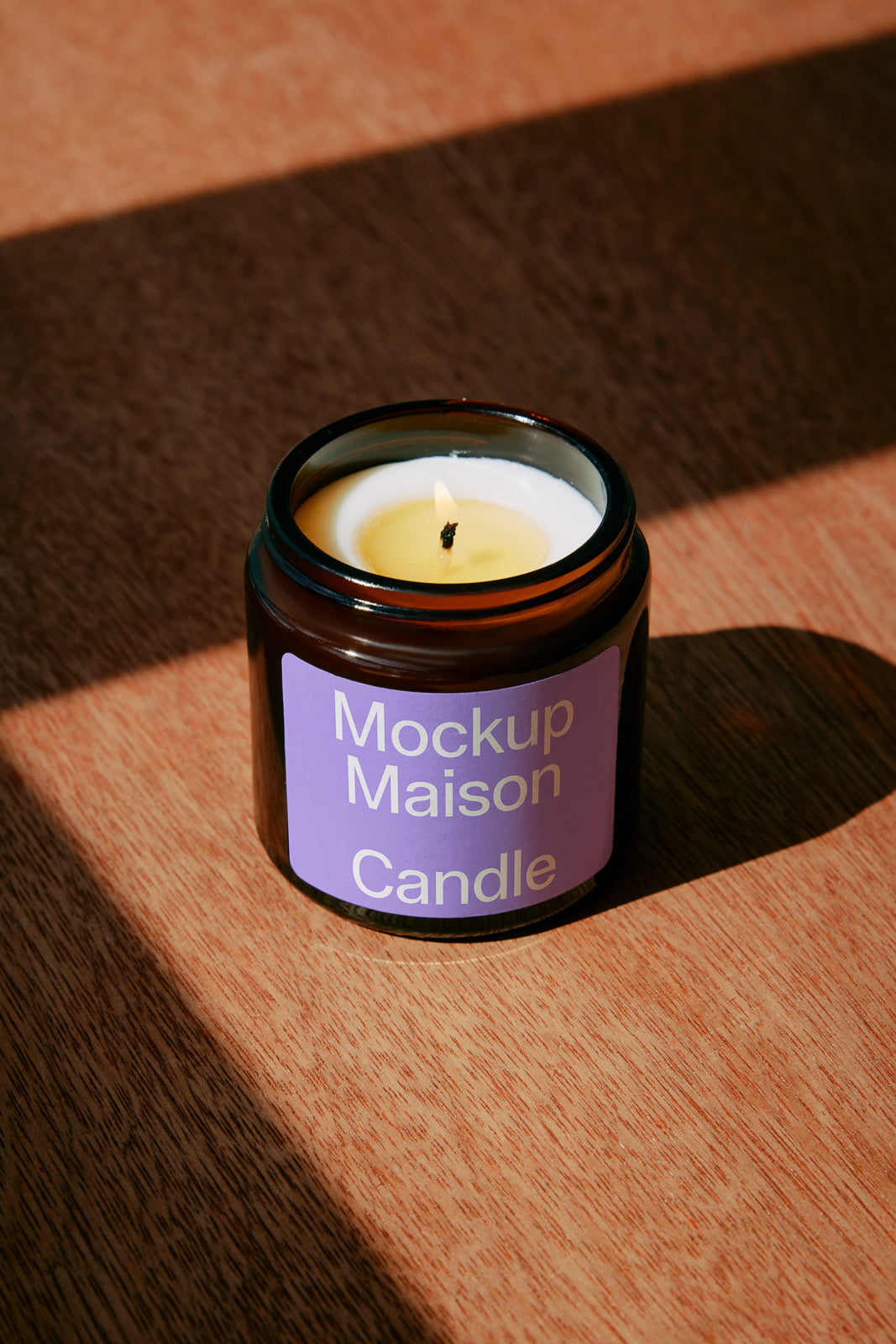 PSD mockup of a lit candle in a dark glass jar labeled "Mockup Maison Candle" on a wooden surface with a shadow cast.