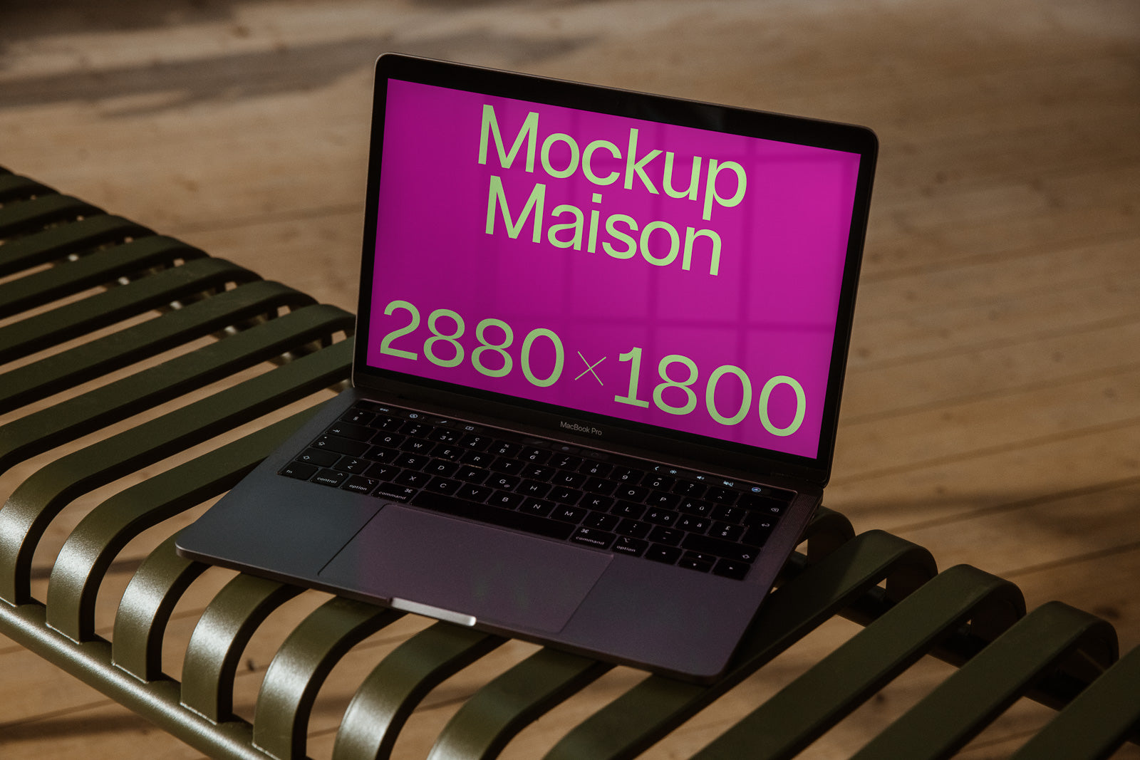 PSD mockup of a laptop on a metal bench with a pink screen displaying text "Mockup Maison" and resolution "2880 x 1800".